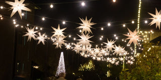Antler Hill Village at night with glowing star lanterns, strings of lights, and an illuminated Christmas tree.⠋