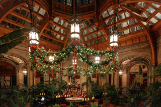 Biltmore House’s Winter Garden decorated with illuminated Christmas garlands and red bows, with a choir gathered behind the Boy with Geese sculpture.