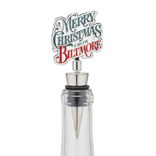 A Christmas-themed wine bottle stopper featuring a silver metal cap and a decorative top sign that reads 'Merry Christmas from Biltmore' in white, teal, and red lettering, shown on a clear glass bottle against a white background.