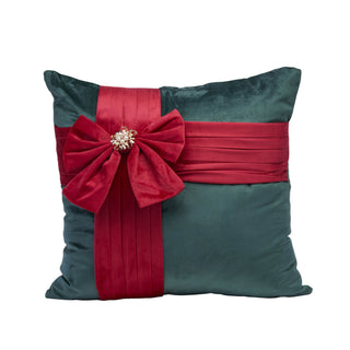 A square dark teal velvet pillow decorated with a wide red sash across the front, a large matching red bow, and a jeweled brooch at the bow's center, shown on a plain white background.