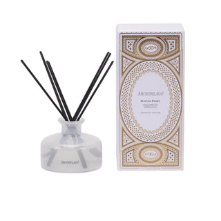 An Archipelago Winter Frost reed diffuser bottle with black reeds and frosted white glass body and gold cap, shown next to its ornate white and gold patterned packaging box on a white background.