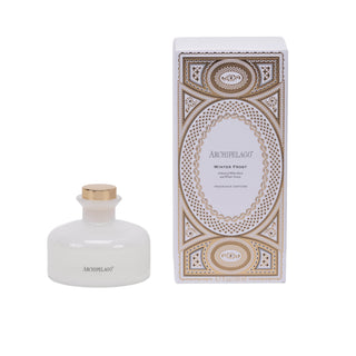 An Archipelago Winter Frost reed diffuser bottle with a frosted white glass body and gold cap, shown next to its ornate white and gold patterned packaging box on a white background.