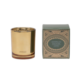 An Archipelago wax candle in a brushed gold metal vessel, shown next to its dark green and gold patterned packaging box on a white background.