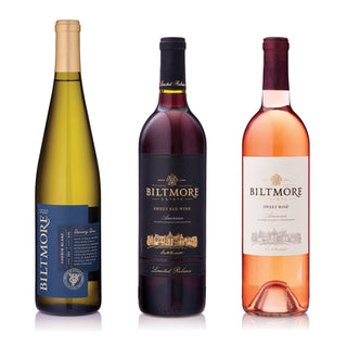 Three Biltmore Estates wine bottles on a white background: a greenish-yellow white wine bottle, a dark red wine bottle with a black label, and a pink rosé wine bottle with a white label.