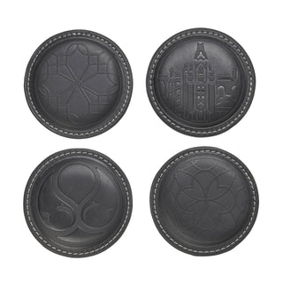Four round dark gray leather coasters arranged in a 2x2 grid on a white background, each featuring a different embossed design including geometric patterns, Biltmore house motif, a stylized monogram, and a floral motif.
