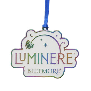 A Luminere Biltmore ornament featuring a white background with an iridescent flower, lettering, and a blue hanging ribbon, shown on a plain white background.