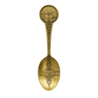 A vintage-style gold-colored metal spoon featuring an embossed circular architectural design on the bowl and a decorative handle with the word 'Biltmore' on the spoon bowl, shown against a plain white background.