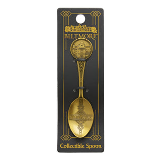 A collectible spoon in a gold finish with Biltmore-themed engravings, mounted on a black display card with gold lettering.