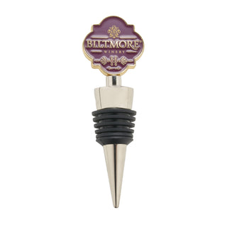 A Biltmore Winery wine stopper with a mauve and gold enamel top, a silver metal cone-shaped point, and a black rubber seal band in the middle, shown on a plain white background.