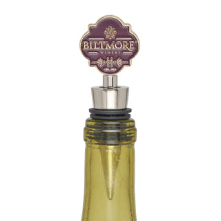 A Biltmore Winery wine bottle stopper with a mauve and gold decorative top, inserted into a yellow-green glass bottle against a white background.