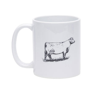 A white ceramic mug with a black line art illustration of a cow standing on grass, shown against a plain white background.