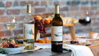 Two bottles of Biltmore Estate winery Christmas wines, one white and one red, displayed on a rustic table with food and wine glasses.