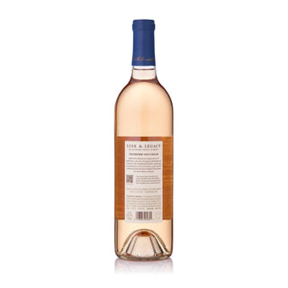 A bottle of Line & Legacy by Biltmore Estate Winery North Carolina Rosé 2025 shown from the back, featuring a salmon-pink hue wine, a cream-colored label including winery story, and a dark blue foil capsule at the neck, set against a plain white background.